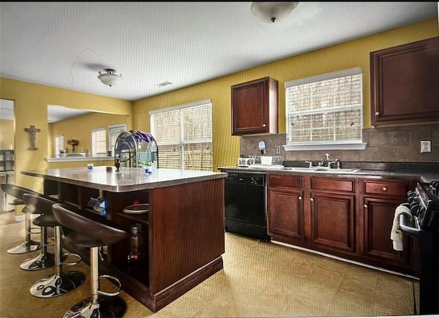 kitchen featuring backsplash, sink, a center island with sink, dishwasher, and stainless steel range with electric cooktop