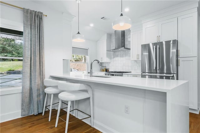 kitchen featuring wall chimney exhaust hood, decorative light fixtures, stainless steel fridge, white cabinets, and sink