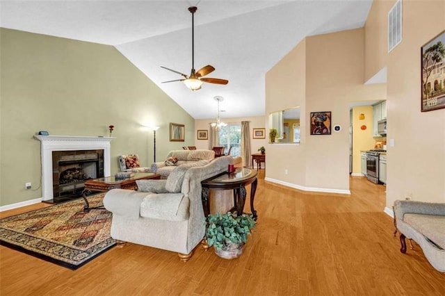 living area featuring visible vents, light wood-style floors, high vaulted ceiling, a tile fireplace, and ceiling fan with notable chandelier