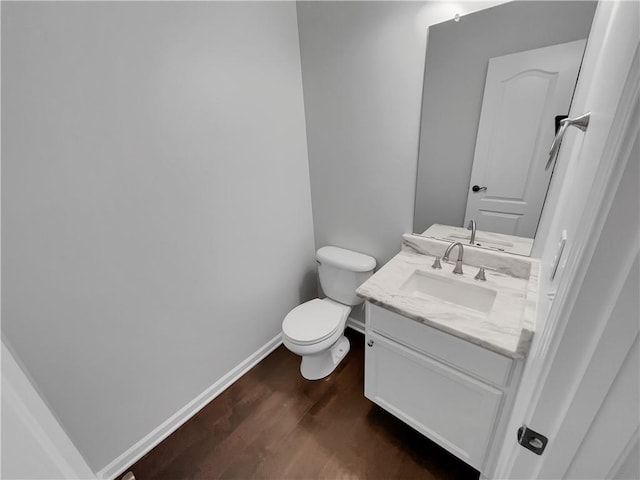 half bath featuring toilet, wood finished floors, vanity, and baseboards