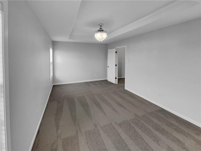 carpeted spare room featuring baseboards, a raised ceiling, and a notable chandelier