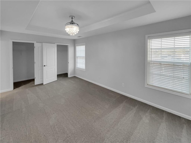 unfurnished bedroom featuring carpet floors, a tray ceiling, and baseboards