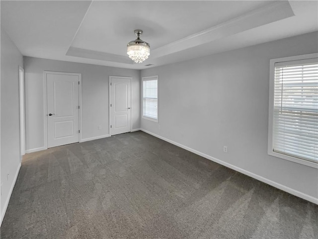 unfurnished bedroom featuring a tray ceiling, a notable chandelier, dark carpet, and baseboards