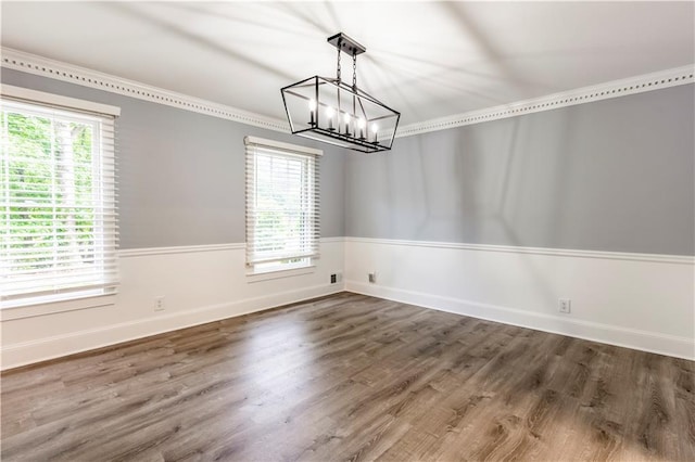 unfurnished dining area featuring a chandelier, wood finished floors, baseboards, and wainscoting