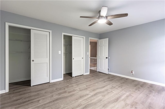 unfurnished bedroom with two closets, wood finished floors, baseboards, and a ceiling fan