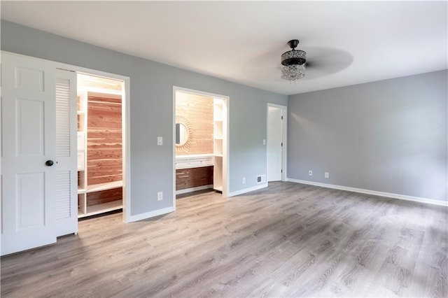 unfurnished bedroom featuring ensuite bathroom, baseboards, wood finished floors, and ceiling fan