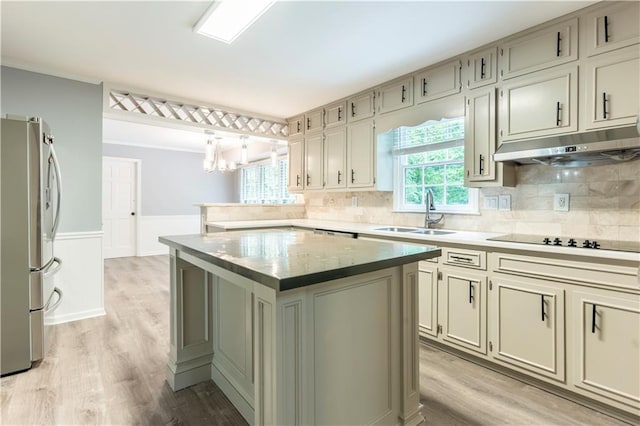kitchen featuring a sink, under cabinet range hood, freestanding refrigerator, black electric cooktop, and tasteful backsplash