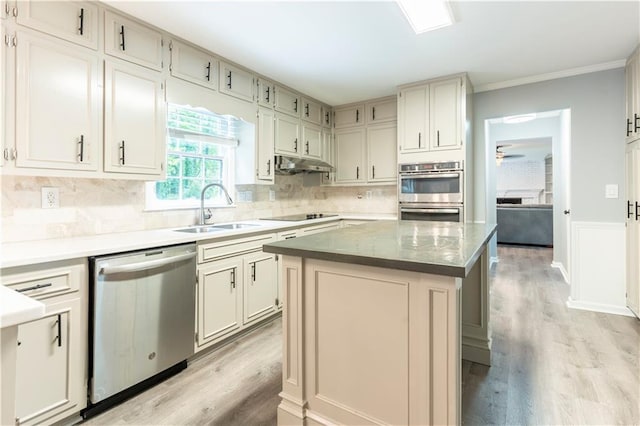 kitchen with appliances with stainless steel finishes, a sink, light wood-type flooring, crown molding, and under cabinet range hood