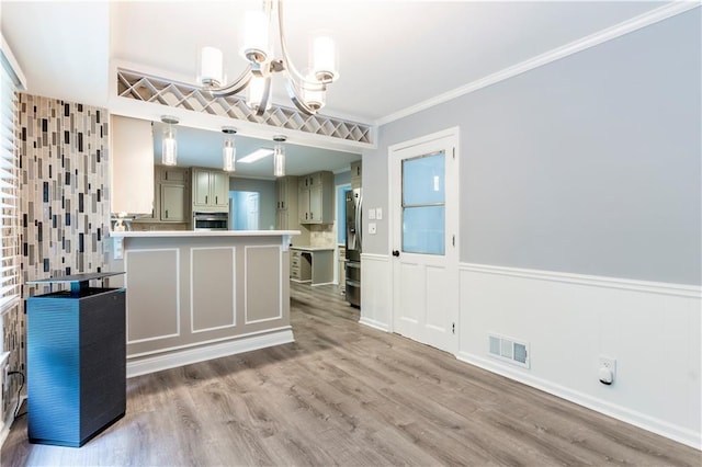 unfurnished dining area with a chandelier, a wainscoted wall, ornamental molding, and wood finished floors