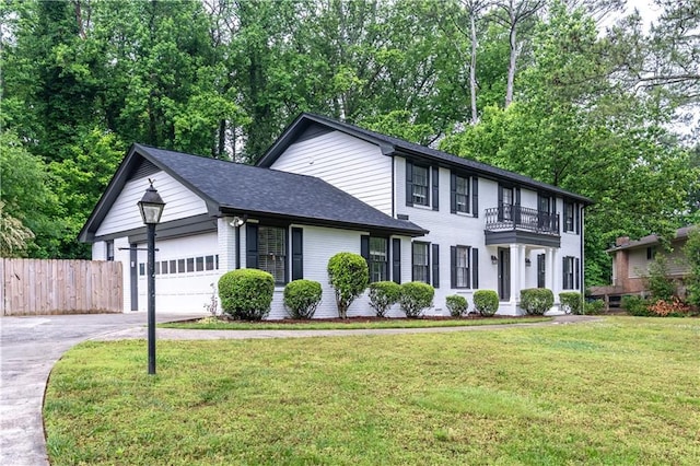 colonial-style house with asphalt driveway, a balcony, a garage, a shingled roof, and view of wooded area