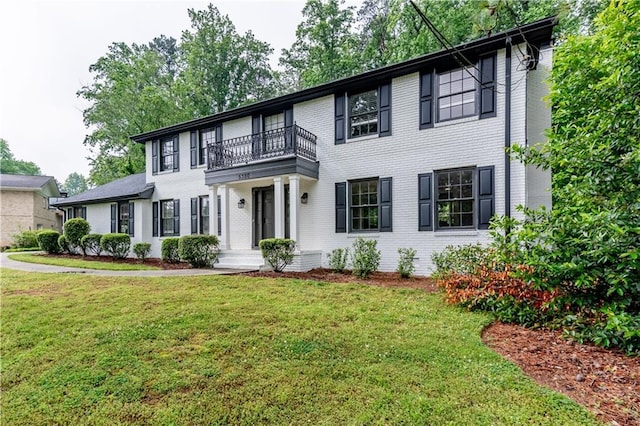 colonial house with a balcony, brick siding, and a front lawn