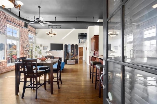 dining room with hardwood / wood-style flooring, ceiling fan with notable chandelier, and brick wall