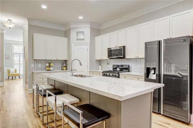 kitchen with appliances with stainless steel finishes, white cabinetry, a kitchen bar, ornamental molding, and a center island with sink