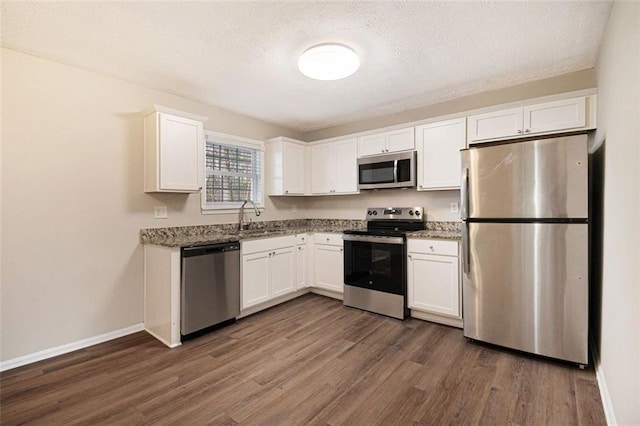 kitchen featuring stainless steel appliances, sink, white cabinets, dark stone countertops, and dark hardwood / wood-style floors