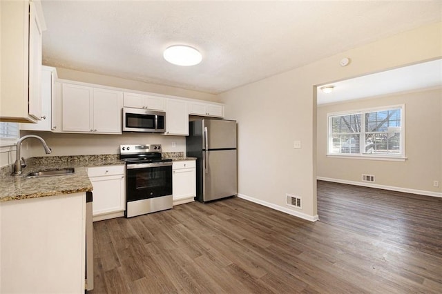 kitchen with stainless steel appliances, sink, white cabinets, light stone countertops, and dark wood-type flooring