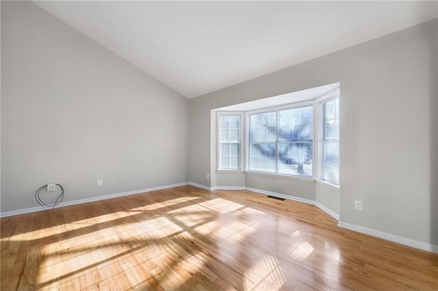 spare room featuring lofted ceiling and light hardwood / wood-style flooring