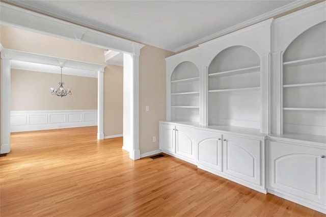 unfurnished dining area featuring crown molding, built in features, light hardwood / wood-style floors, and a chandelier