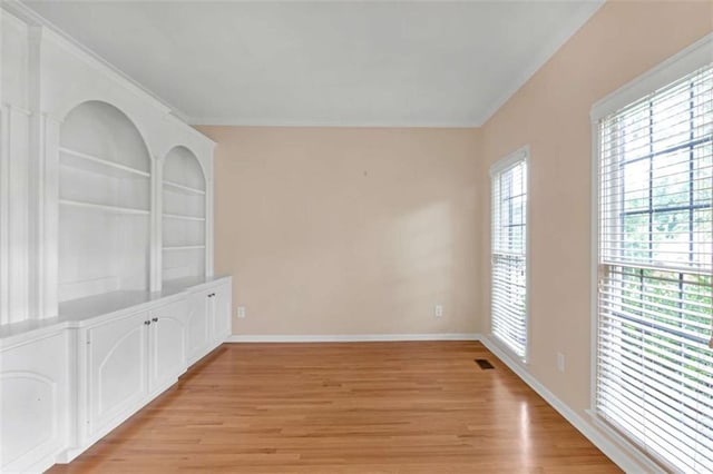 empty room with crown molding, light wood-type flooring, and built in shelves