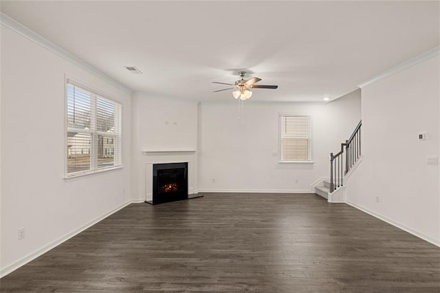 1159 Blue Juniper Cir, Loganville, GA 30052 - unfurnished living room with a ceiling fan, crown molding, a warm lit fireplace, stairs, and dark wood-style flooring