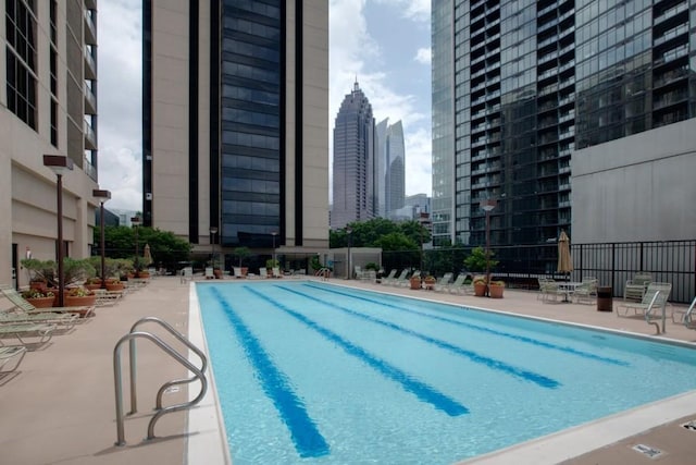 community pool featuring a view of city, a patio, and fence