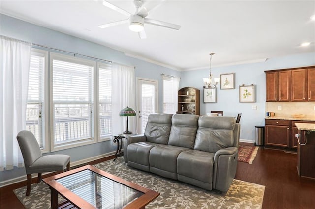 living room featuring ceiling fan with notable chandelier, ornamental molding, baseboards, and dark wood-style flooring