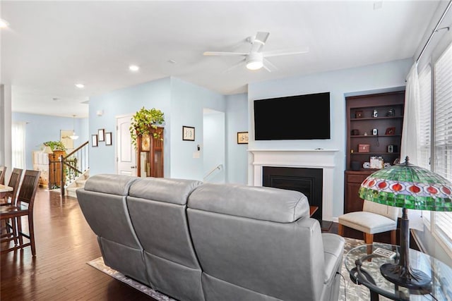 living room featuring stairs, recessed lighting, a fireplace, wood finished floors, and a ceiling fan