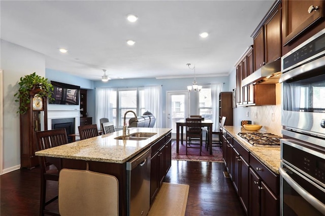 kitchen featuring a breakfast bar area, dark wood-style floors, a sink, under cabinet range hood, and appliances with stainless steel finishes