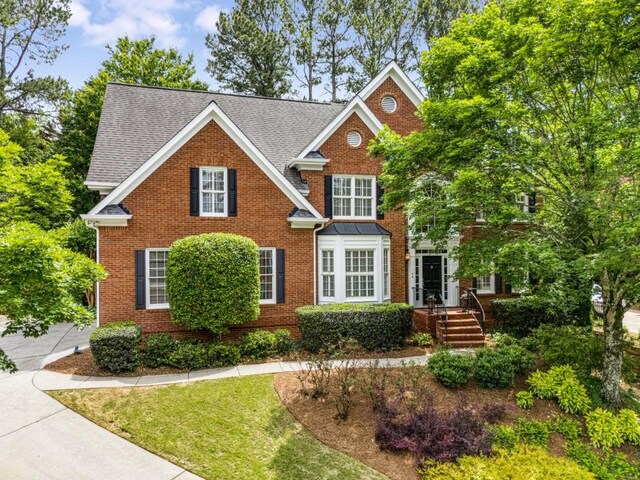 view of front of home featuring brick siding, a front lawn, and roof with shingles