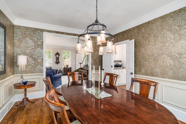 dining room with wood finished floors, wallpapered walls, a wainscoted wall, ornamental molding, and a chandelier