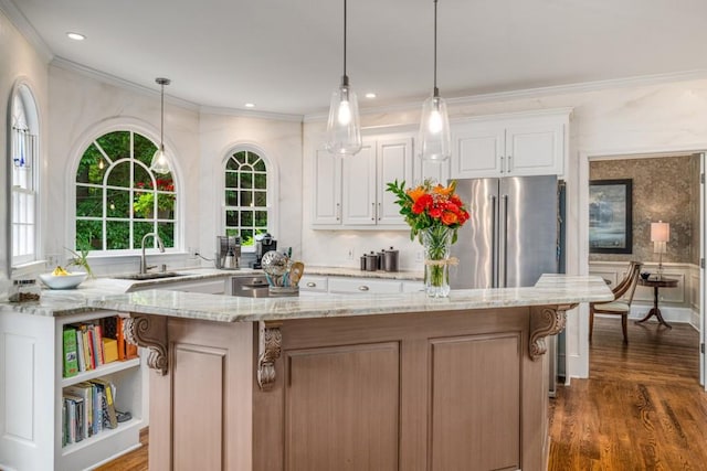 kitchen featuring a sink, high quality fridge, ornamental molding, light stone counters, and a center island