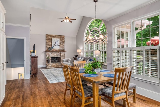 dining room with ceiling fan, wood finished floors, a stone fireplace, baseboards, and crown molding