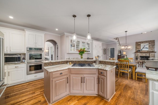 kitchen featuring stainless steel appliances, ornamental molding, wood finished floors, arched walkways, and light stone countertops