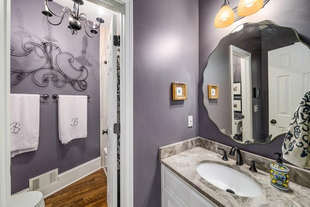 bathroom featuring toilet, wood finished floors, vanity, and a chandelier