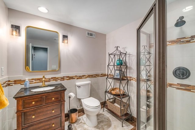 full bath with tile walls, toilet, vanity, a tile shower, and wainscoting