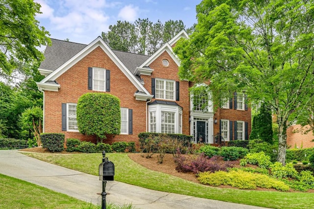 colonial-style house with brick siding, a front yard, and a shingled roof