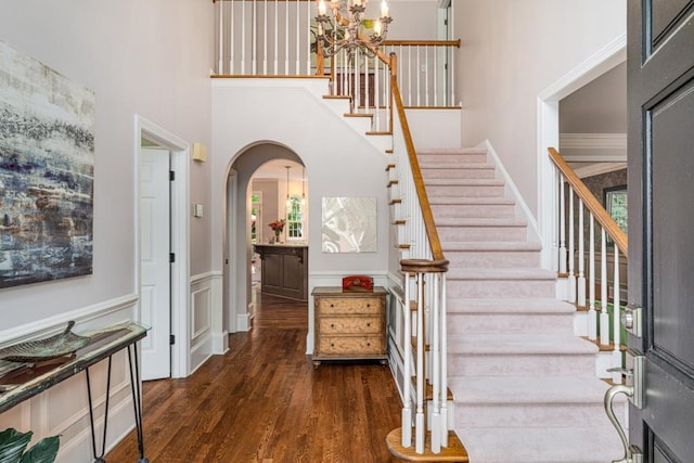 stairs featuring arched walkways, a high ceiling, wood finished floors, a chandelier, and healthy amount of natural light