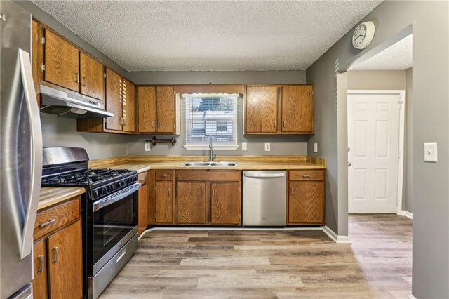 kitchen with a textured ceiling, light hardwood / wood-style floors, sink, and stainless steel appliances