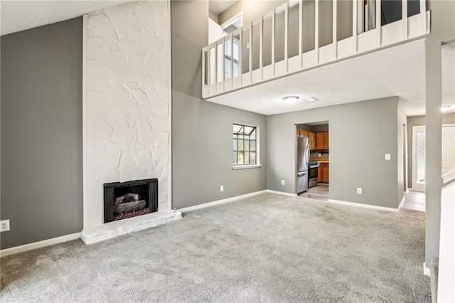 unfurnished living room featuring a stone fireplace, baseboards, and carpet