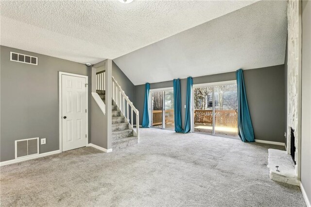 unfurnished living room with carpet, a stone fireplace, lofted ceiling, and a textured ceiling