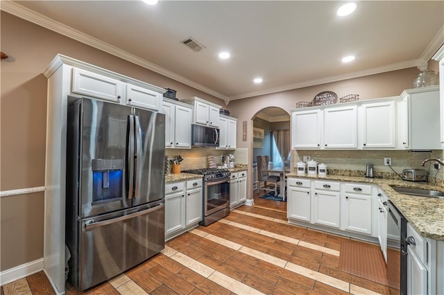 kitchen featuring visible vents, arched walkways, tasteful backsplash, a sink, and appliances with stainless steel finishes