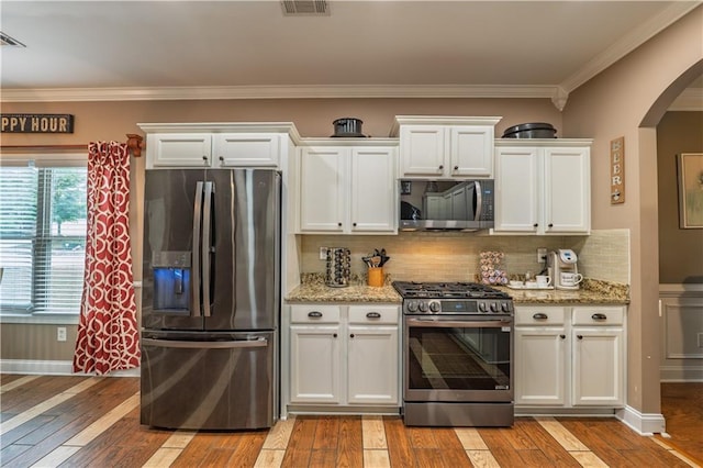 kitchen with visible vents, appliances with stainless steel finishes, arched walkways, light wood finished floors, and ornamental molding