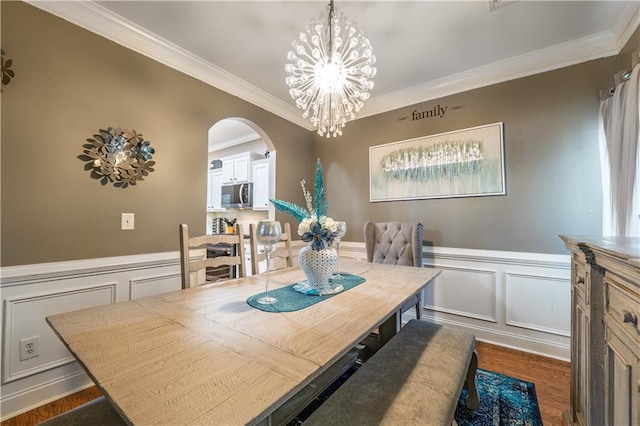 dining area featuring arched walkways, an inviting chandelier, ornamental molding, and a decorative wall