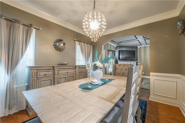 dining space with arched walkways, wood finished floors, a notable chandelier, and ornamental molding