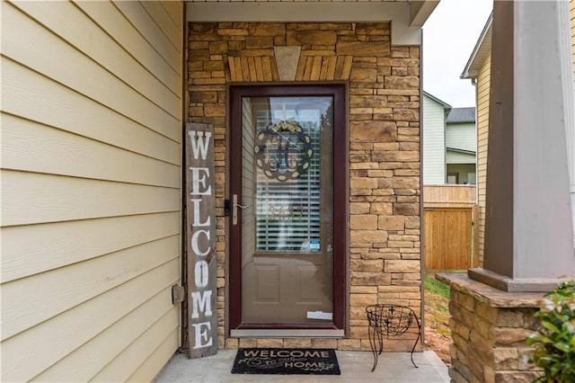 entrance to property featuring fence and stone siding