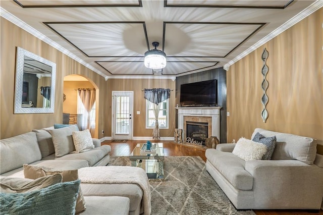 living room with crown molding, arched walkways, a glass covered fireplace, a ceiling fan, and wood finished floors