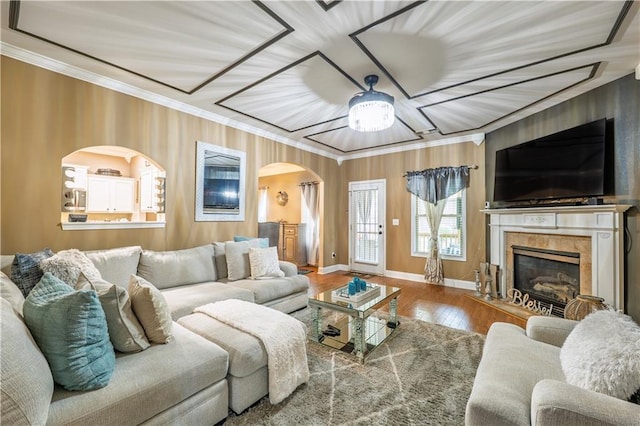 living area featuring ornamental molding, wood finished floors, baseboards, ceiling fan, and arched walkways