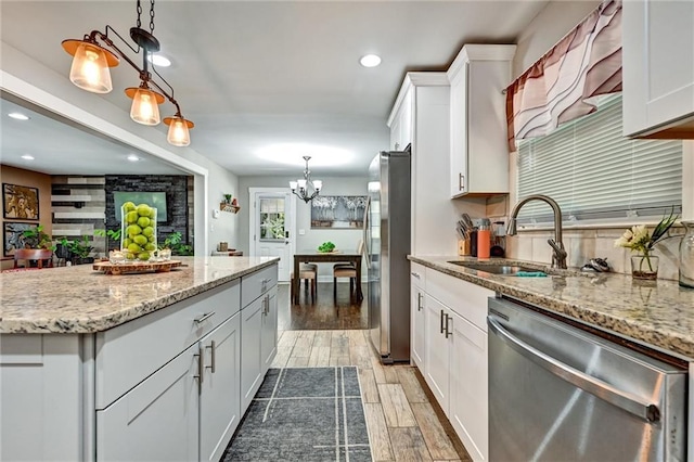 kitchen featuring decorative light fixtures, stainless steel appliances, wood finish floors, white cabinetry, and a sink