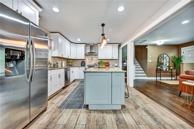 kitchen featuring stainless steel appliances, wood finished floors, white cabinetry, decorative backsplash, and wall chimney exhaust hood