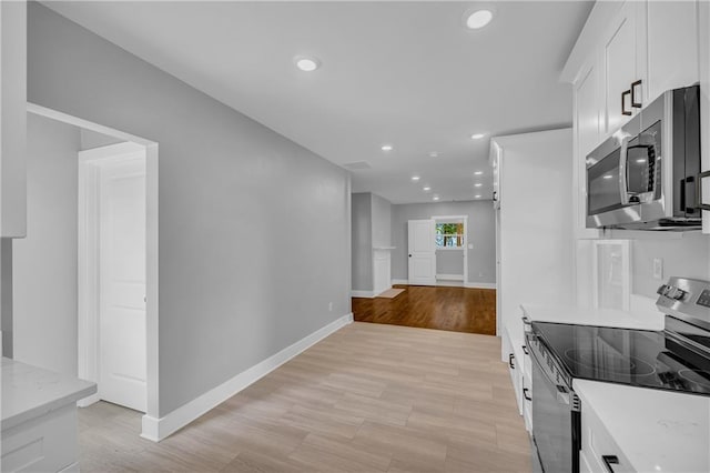 kitchen with light stone counters, white cabinets, light wood-type flooring, and appliances with stainless steel finishes