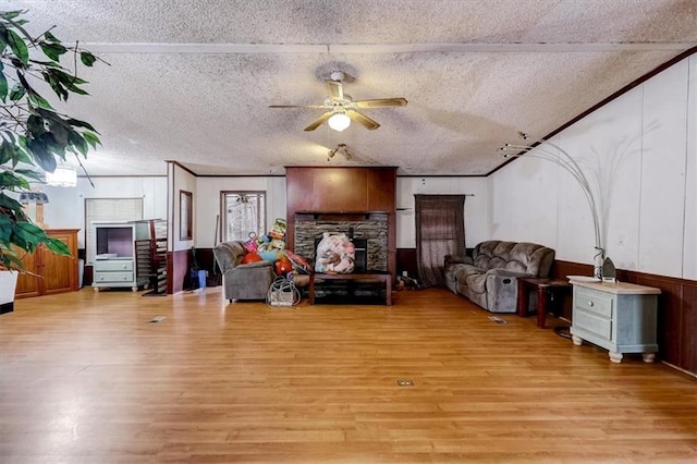 living room featuring ceiling fan, light wood-type flooring, a stone fireplace, and a textured ceiling